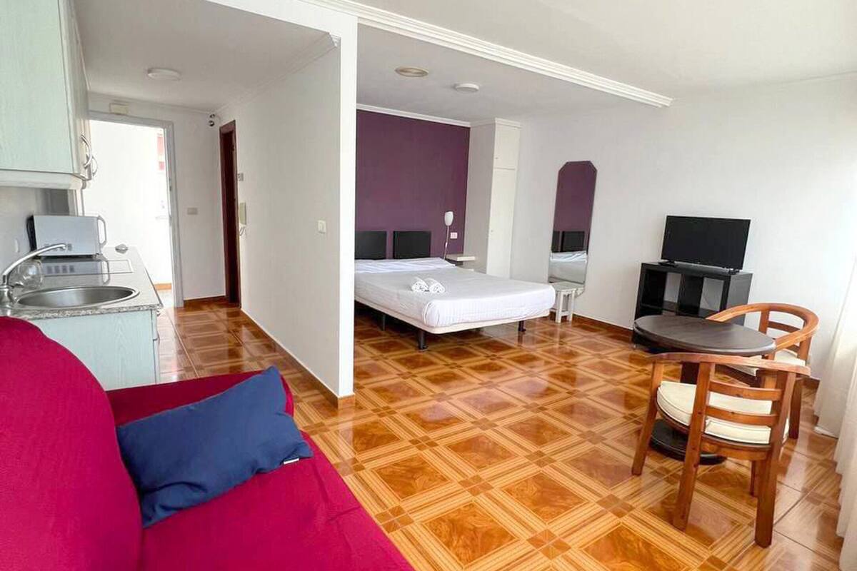 Ein Hotelzimmer mit Holzboden, einer roten Couch, einem Bett mit weißer Matratze, einem Fernseher und einem kleinen Esstisch mit Stuhl.