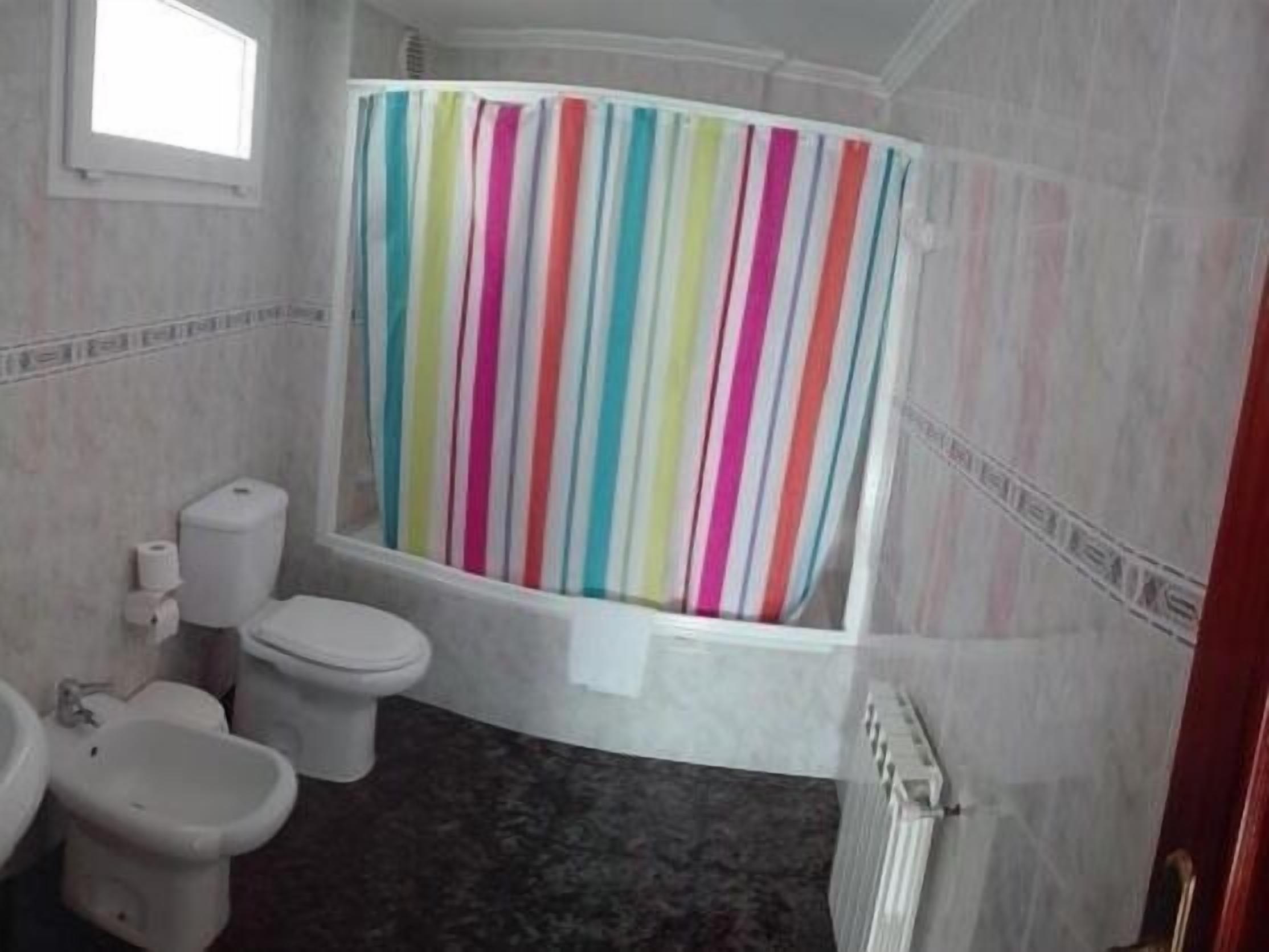 Ein Badezimmer mit gestreifter Duschvorhang, Toilette, Bidet und Heizkörper.