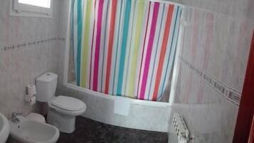 Ein Badezimmer mit gestreifter Duschvorhang, Toilette, Bidet und Heizkörper.