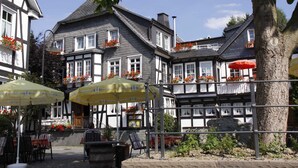 A traditional European building with multiple windows, outdoor seating with umbrellas, and flower boxes on the balconies. - Landhotel Albers (Schmallenberg)