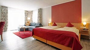 A hotel room with a large bed, a sofa, a red rug, and a teddy bear.