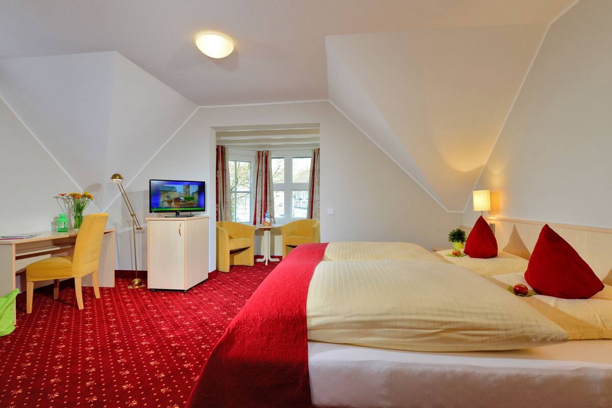 A hotel room with a bed, desk, chair, television, and a window with curtains.