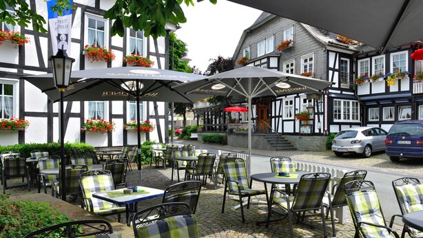 An outdoor café with tables and chairs, surrounded by traditional buildings with flower boxes. - Landhotel Albers (Schmallenberg)
