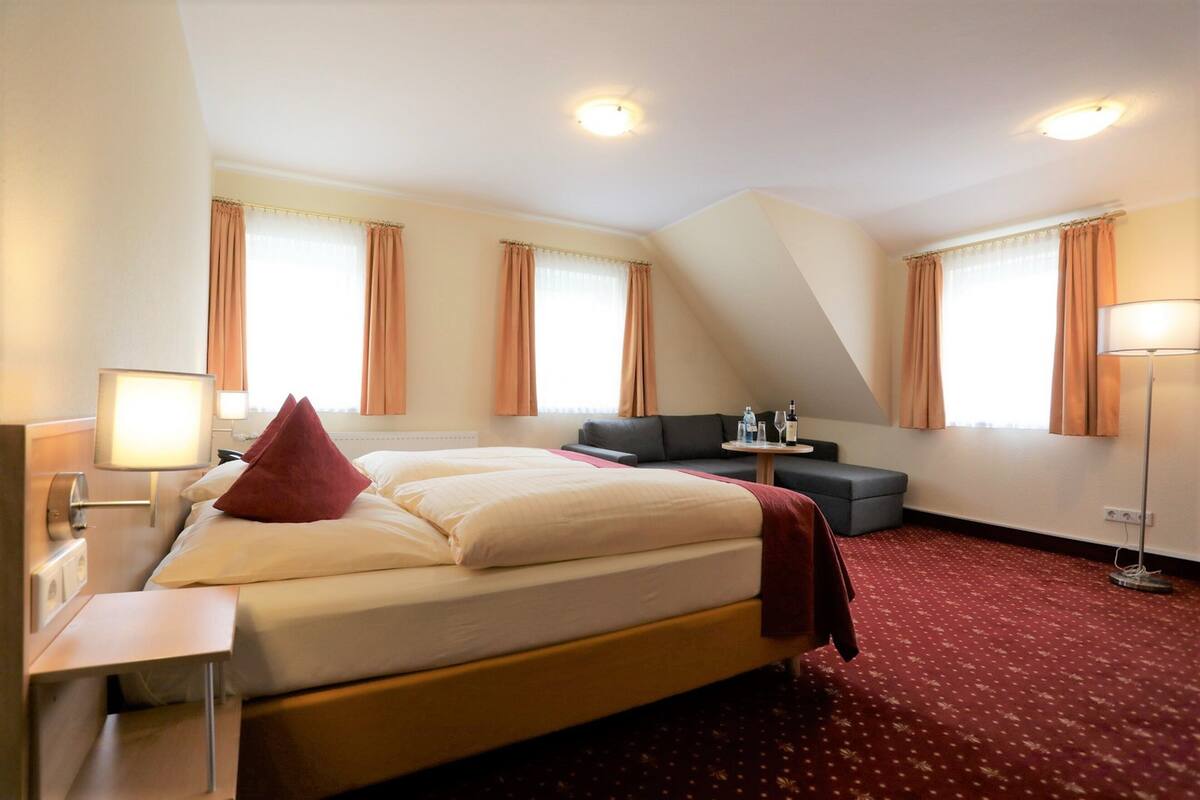 A hotel room with a large bed, a desk, a sofa, and a standing lamp.