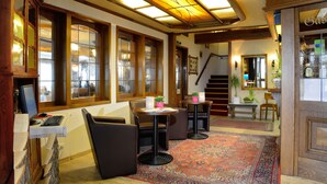 A cozy interior with wooden beams, large windows, a staircase, and a small table with chairs. - Landhotel Albers (Schmallenberg)