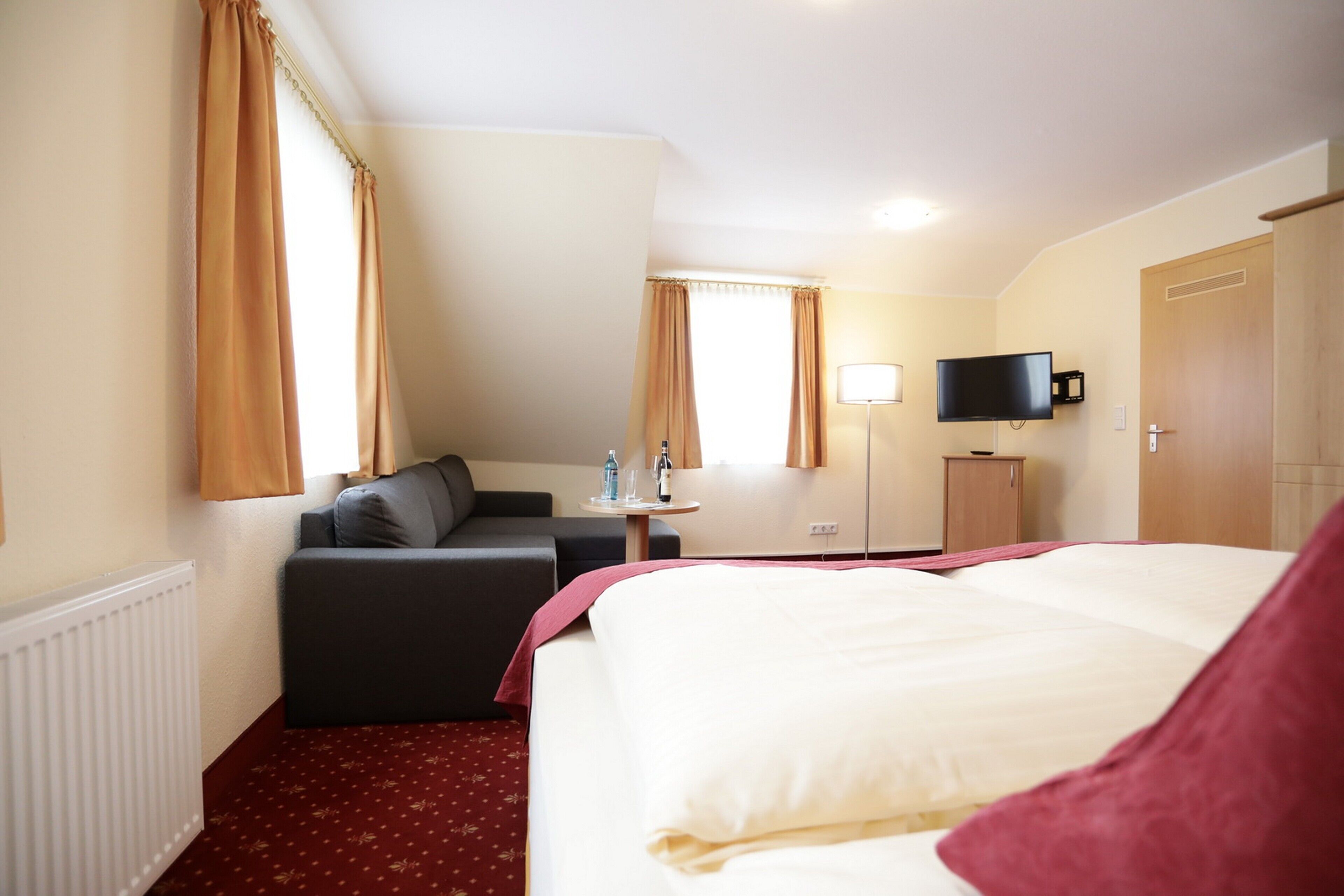 Quarto de hotel com cama, sofá, escrivaninha, televisão e guarda-roupa.