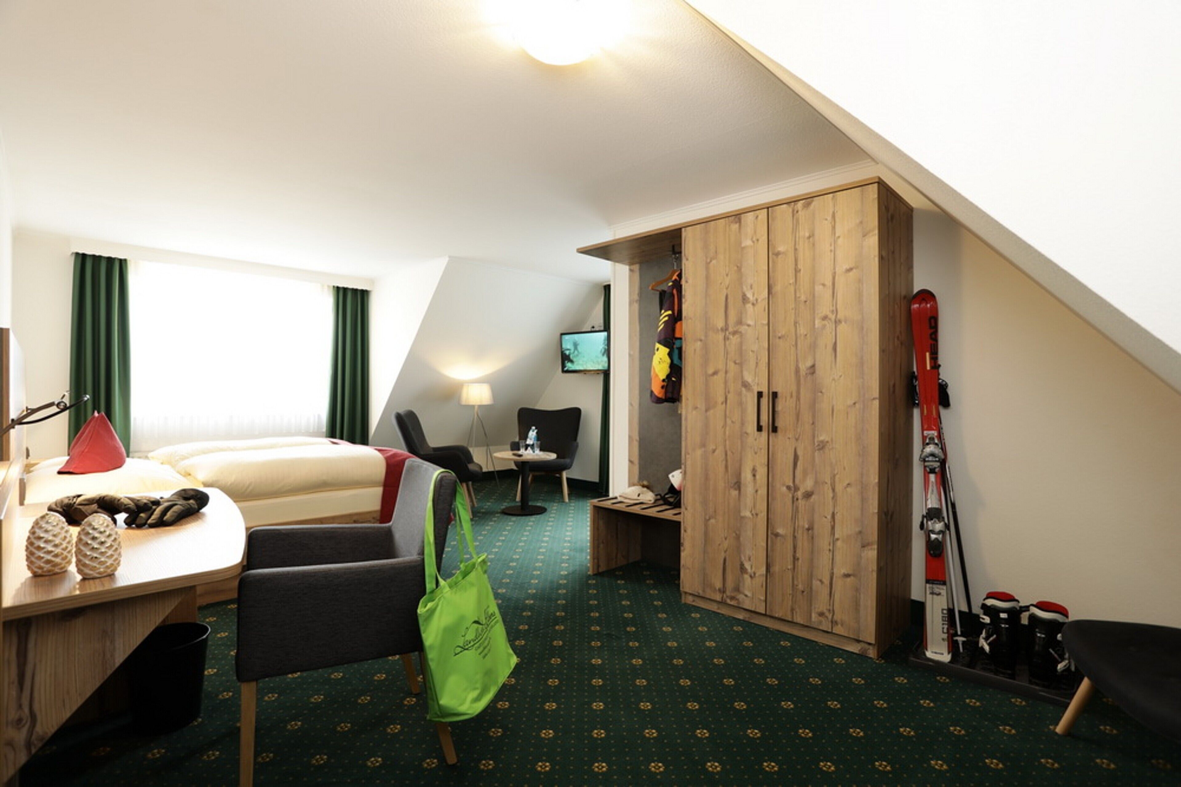 Habitación de hotel con cama, escritorio, silla, armario, equipo de esquí y televisión.
