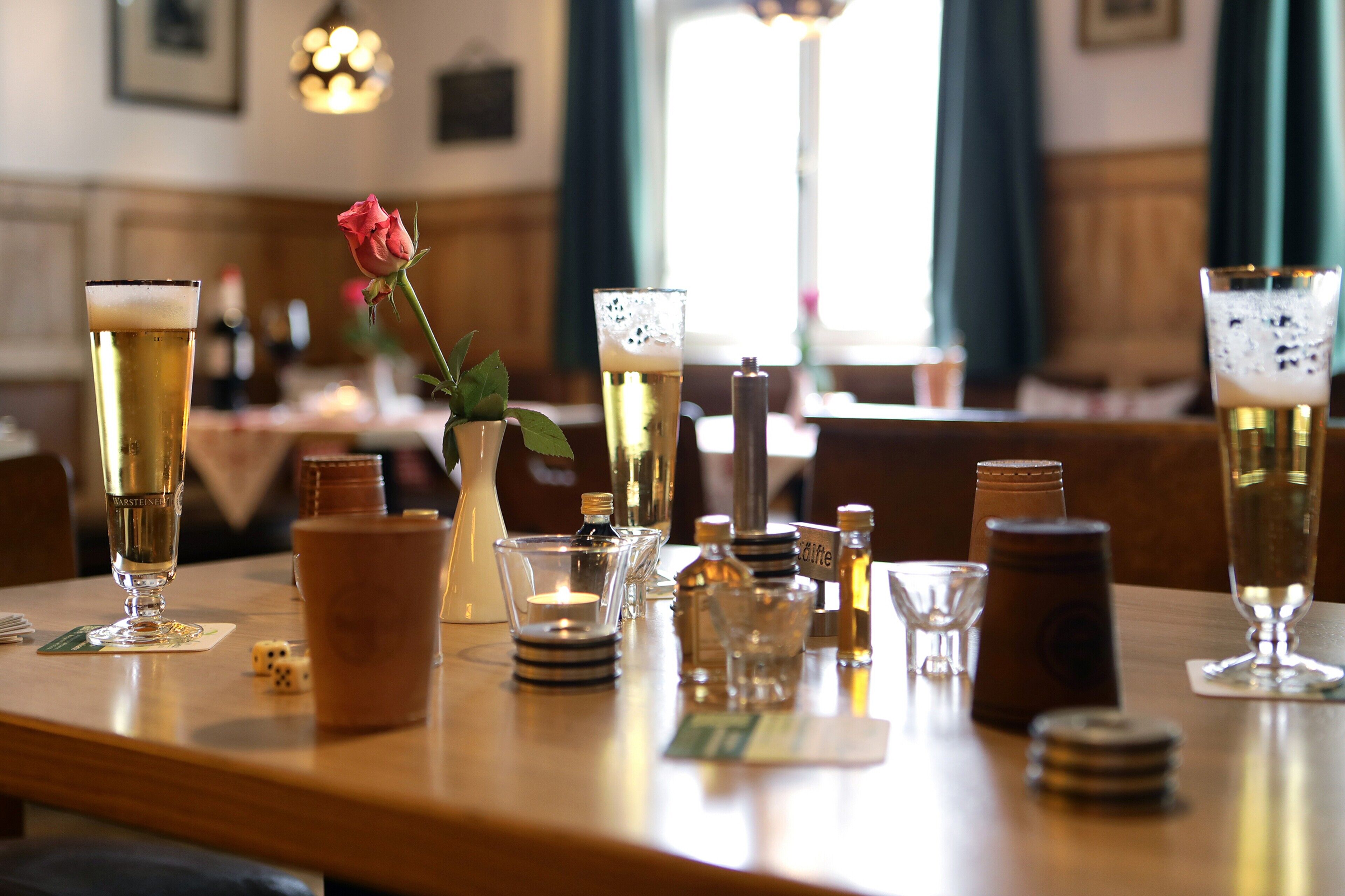 Una mesa de comedor bien dispuesta con diferentes vasos de cerveza, una rosa y pequeños adornos.