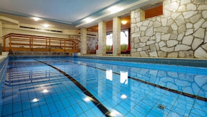 An indoor swimming pool with blue tiles, stone walls, and a wooden railing. - Landhotel Albers (Schmallenberg)