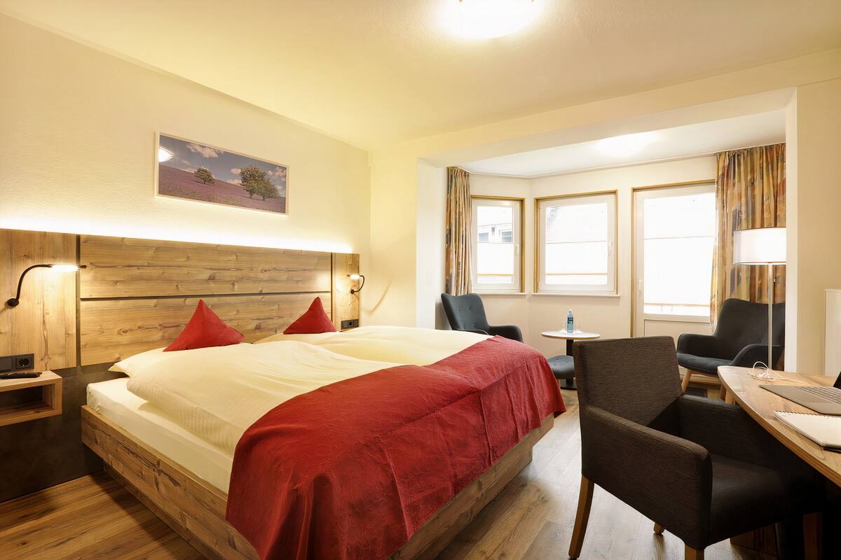 A hotel room with a wooden bed, red pillows, a desk with a laptop, and a chair.