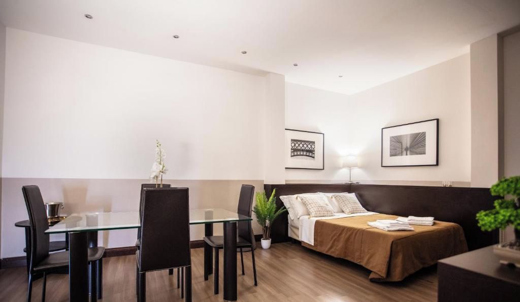 Habitación de hotel con cama, mesita de noche, lámpara y un área de comedor con sillas y una mesa.