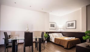 A hotel room with a bed, bedside table, lamp, and a dining area with chairs and a table. - Hotel Boutique Nazionale (Rome)