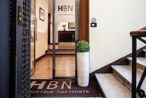 A hotel entrance with a reception desk, a sign reading 'HBN hotel boutique nationale,' and a potted plant. - Hotel Boutique Nazionale (Rome)