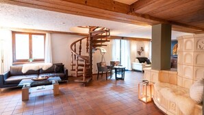 A cozy living room with a wooden spiral staircase, a sofa, a coffee table, and a fireplace. - Hotel Alpenhof (Unterbaech)