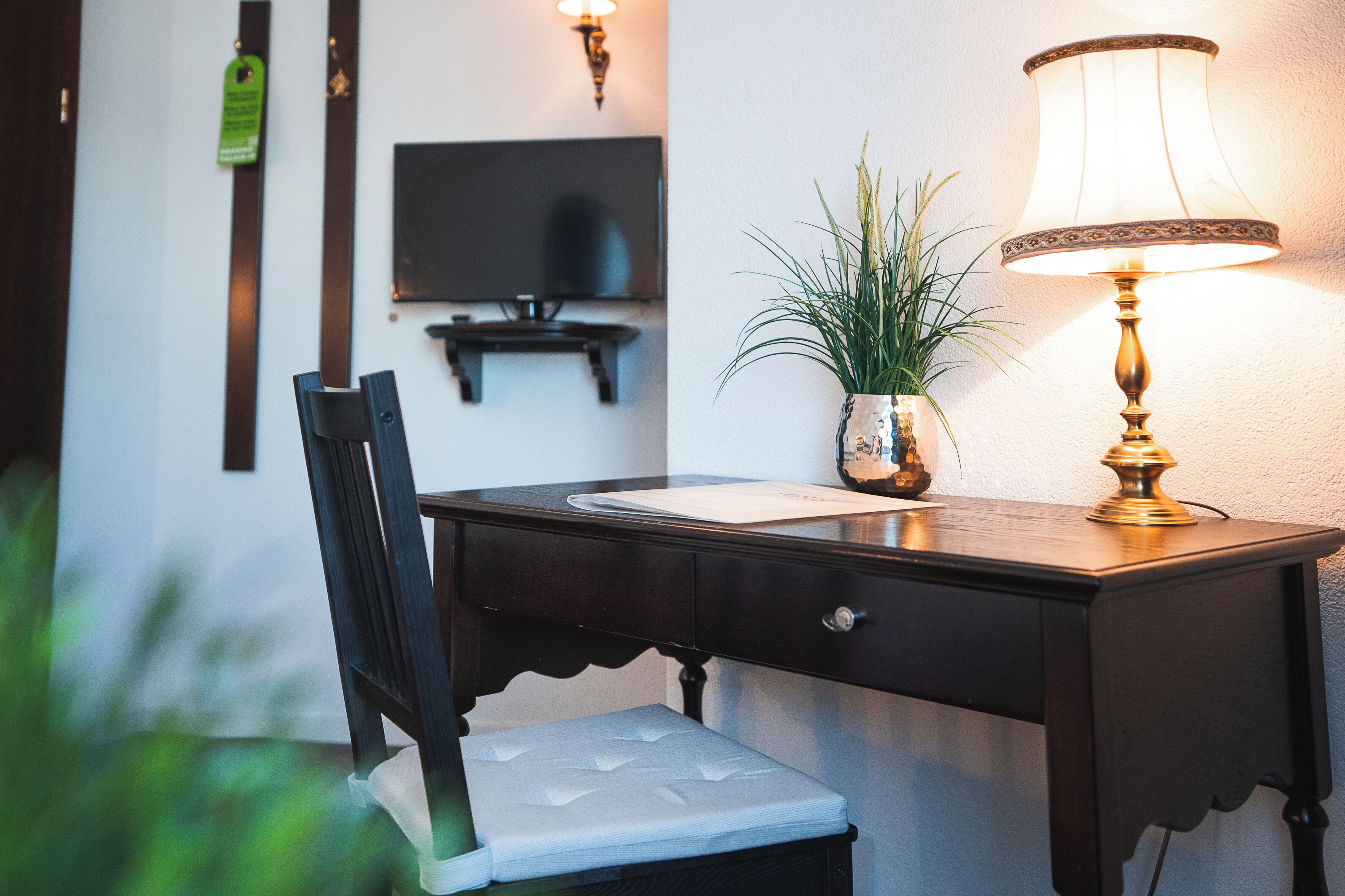 A wooden desk with a lamp, a chair, a television, and a potted plant.