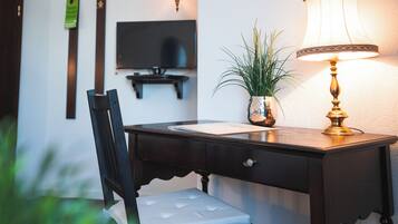 A wooden desk with a lamp, a chair, a television, and a potted plant.