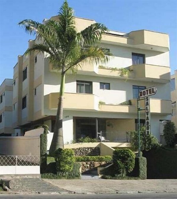 A multi-story hotel with a balcony on the second floor, a palm tree in front, and a sign indicating it is a hotel. - Hotel Salvador (Poços de Caldas)