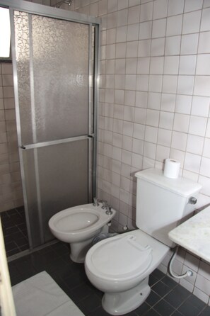 A bathroom with a shower enclosure, two toilets, and a sink. - Hotel Salvador (Poços de Caldas)