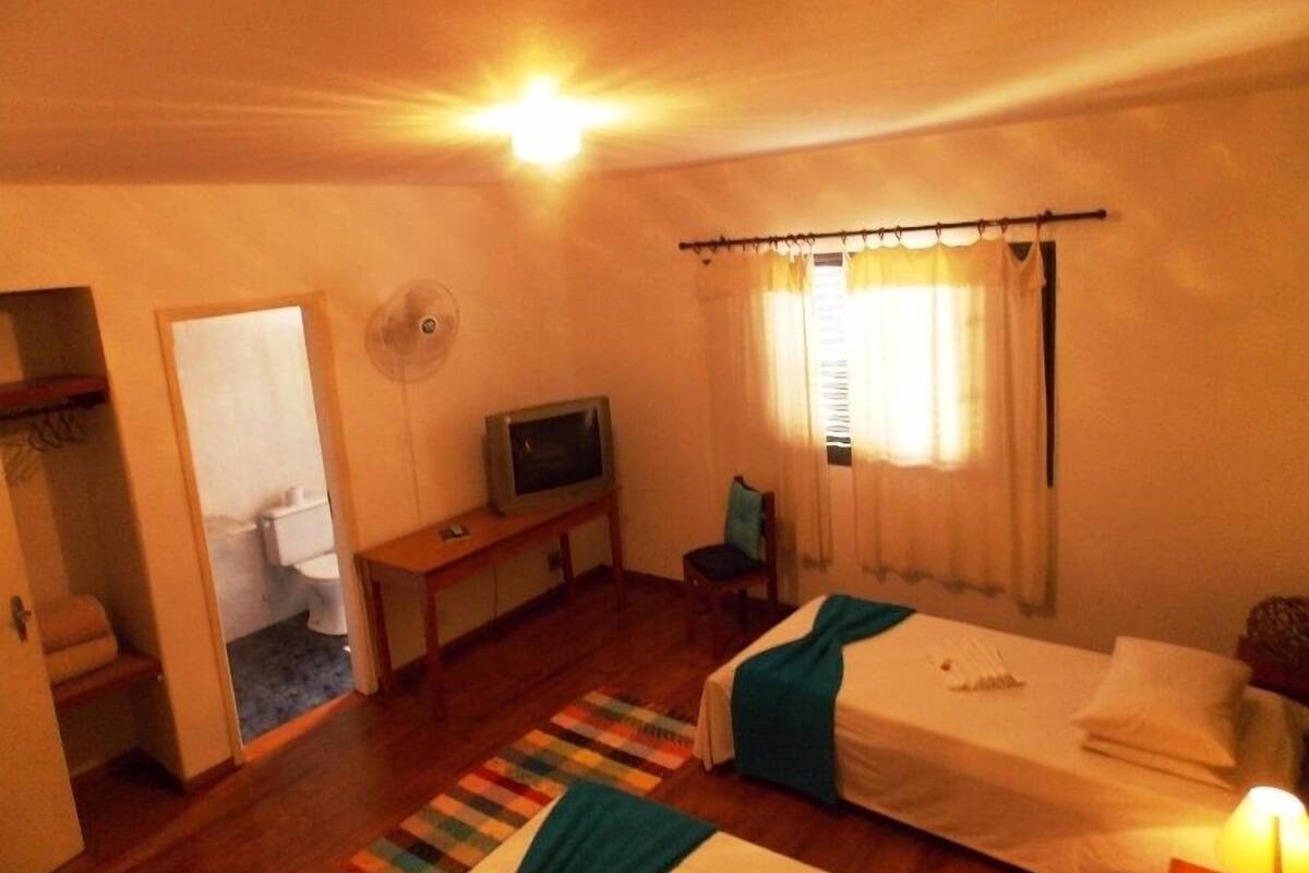 Una habitación pequeña y acogedora con dos camas, un televisor sobre una mesa de madera y un ventanal con cortinas.