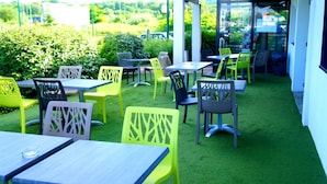 An outdoor seating area with tables and chairs, surrounded by greenery. - Hotel Ibis Budget Metz Sud Augny (Augny)