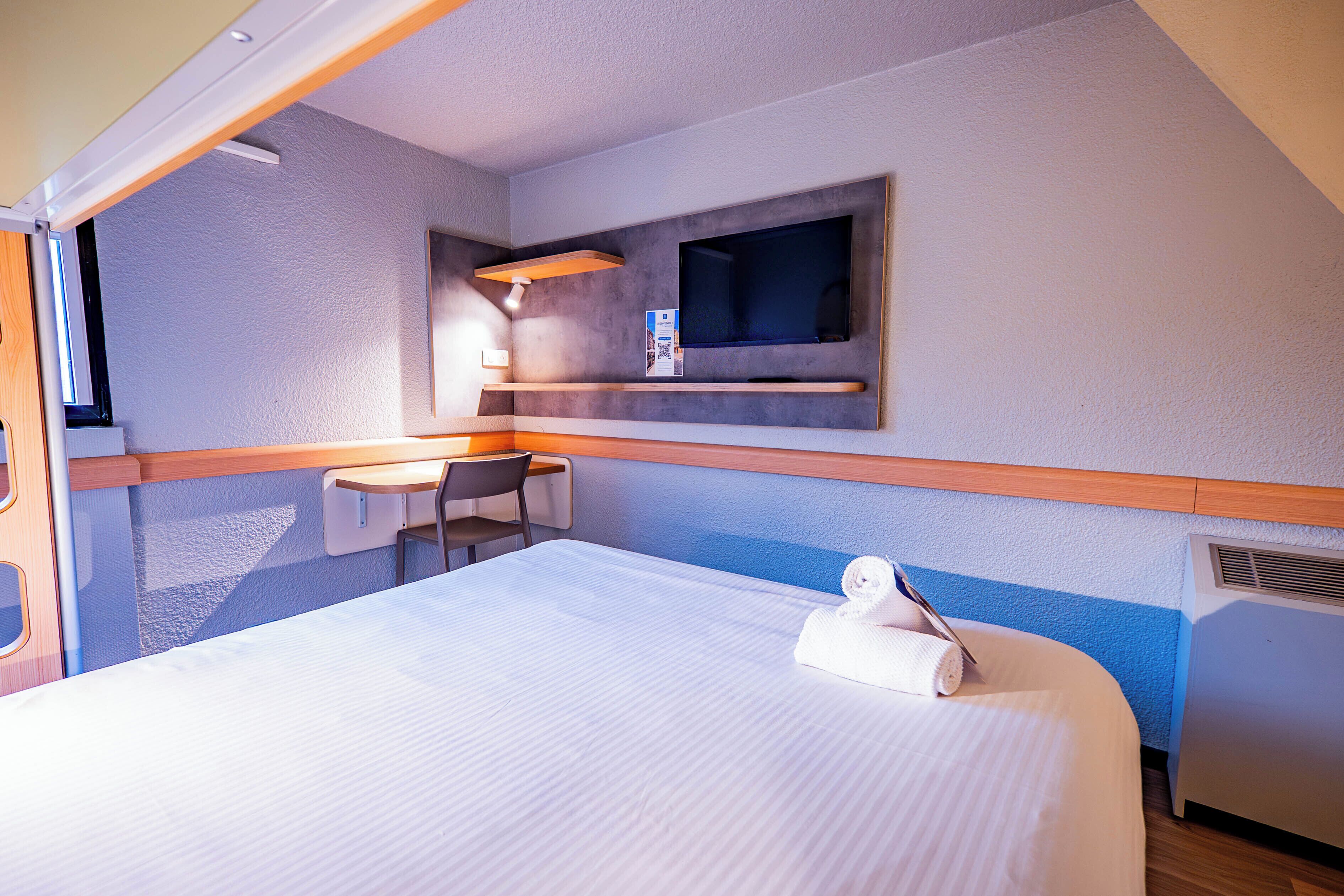 Habitación de hotel con cama, escritorio, silla, televisión de pantalla plana y una mesita.