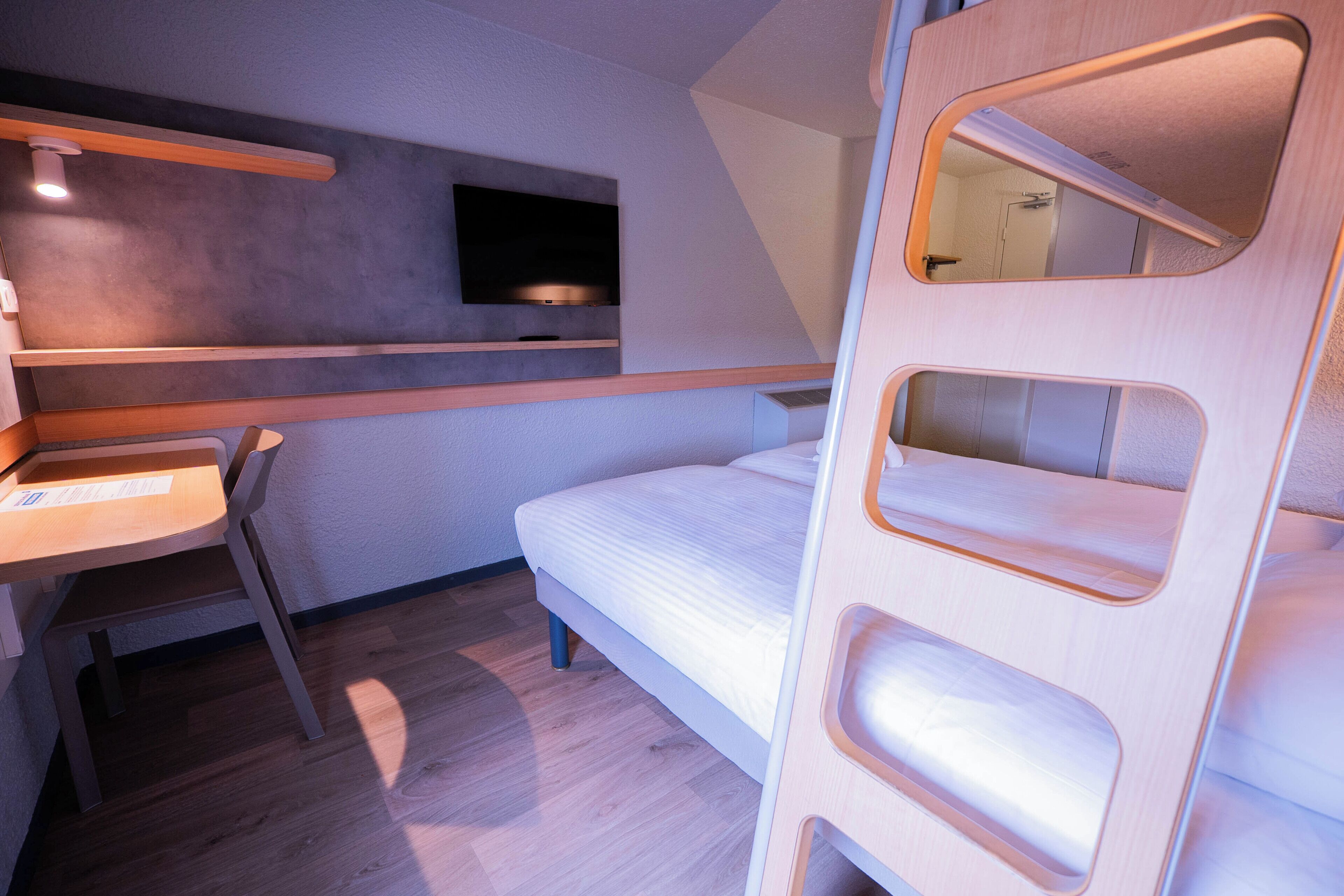 A compact room with a bed, a desk, and a mounted TV.