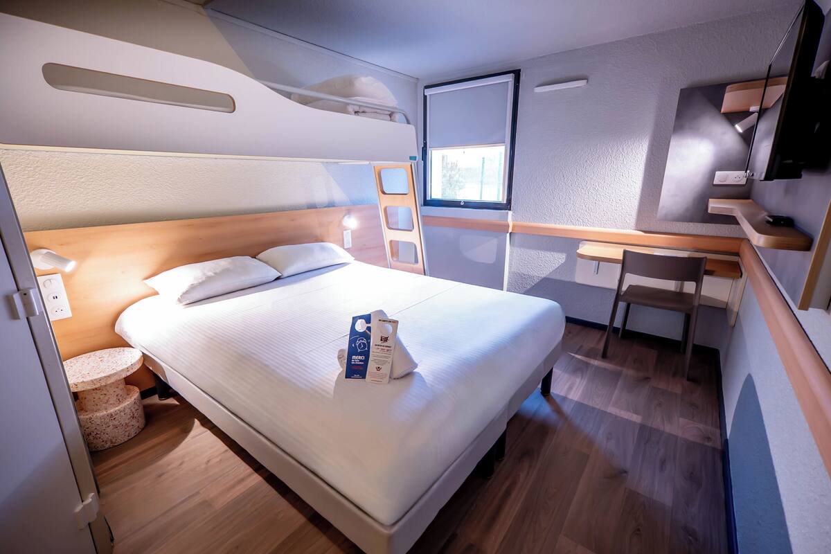 Une chambre d’hôtel de taille modeste, comprenant un lit simple, un bureau, une chaise, une télévision et une fenêtre.