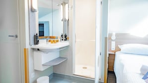 A modern hotel bathroom with a shower, sink, and mirror. - Hotel Ibis Budget Metz Sud Augny (Augny)