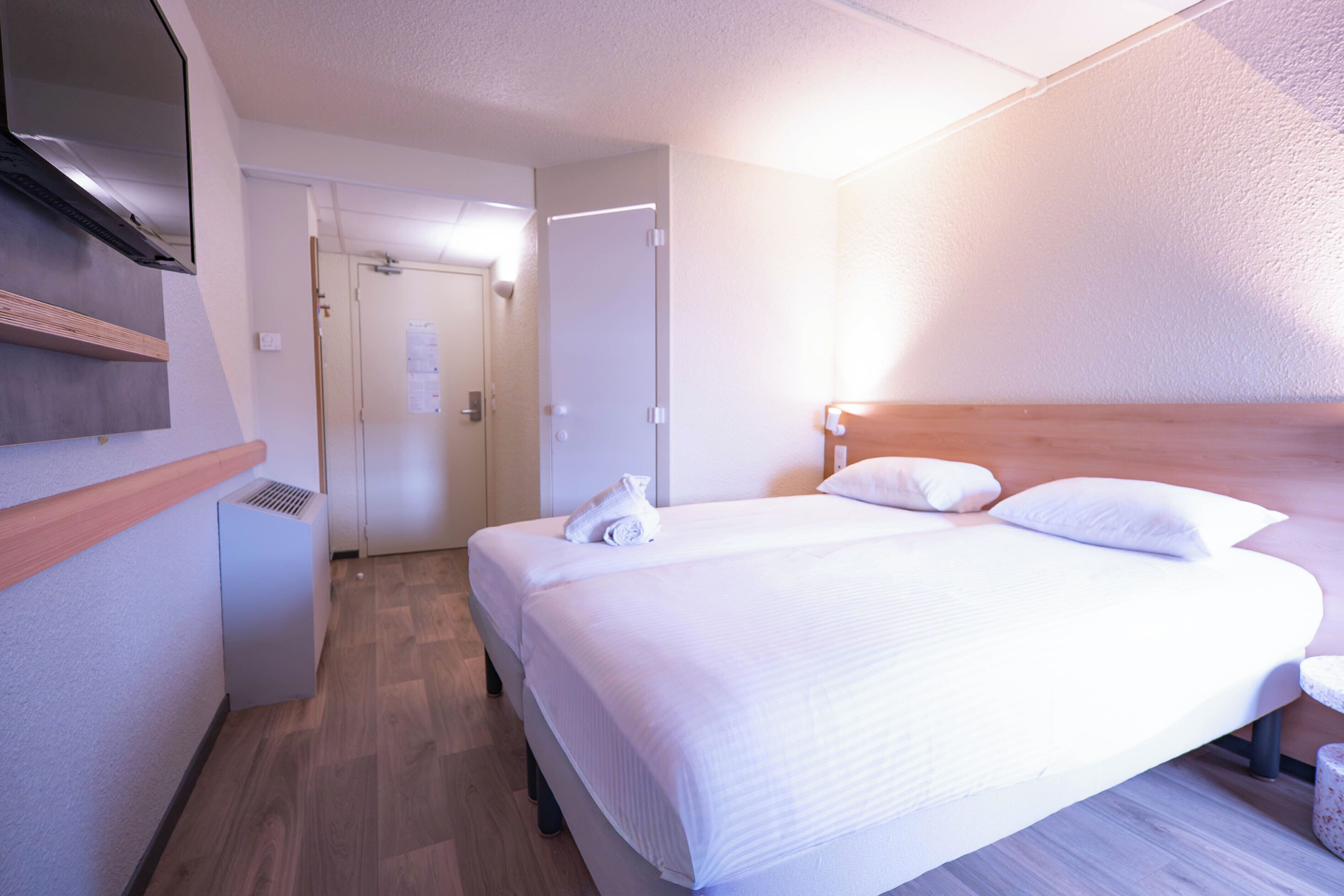 A hotel room with a bed, a bedside table, a wall-mounted TV, and a door leading to a bathroom.