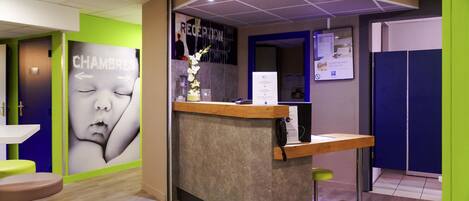 A reception area with a reception desk, a wall with a large portrait, a green mat on the floor, and a blue wall with a poster.