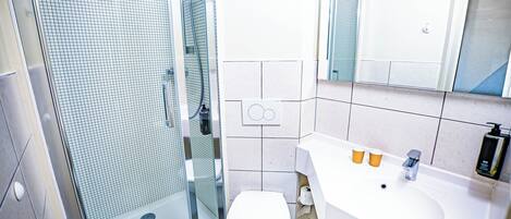 Un baño moderno con cabina de ducha de vidrio, inodoro blanco y lavamanos con dos vasos.
