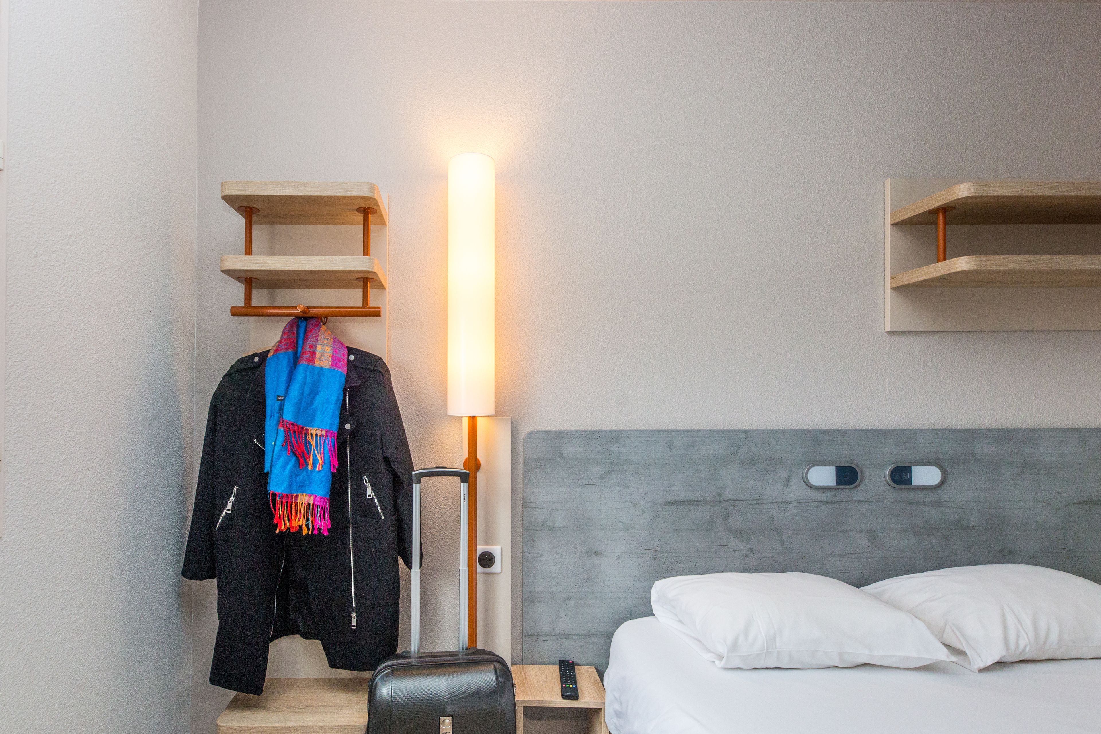 A hotel room with a bed, a nightstand, a lamp, a wardrobe, and a hanging coat.
