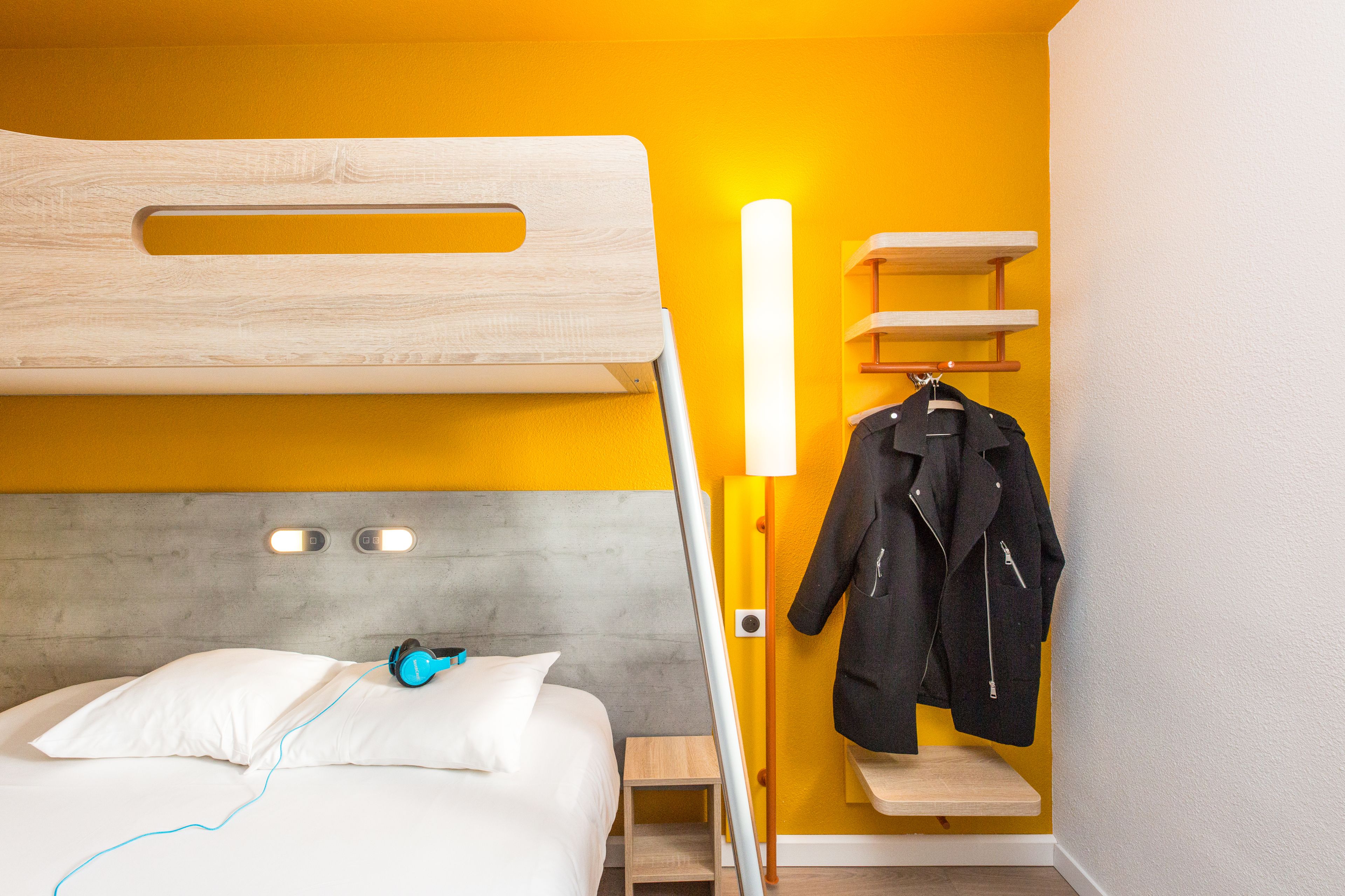 Ein Zimmer mit Etagenbett, Nachttisch, Lampe und Kleiderhaken mit Jacke.