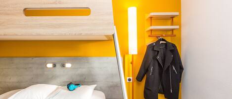 Ein Zimmer mit Etagenbett, Nachttisch, Lampe und Kleiderhaken mit Jacke.
