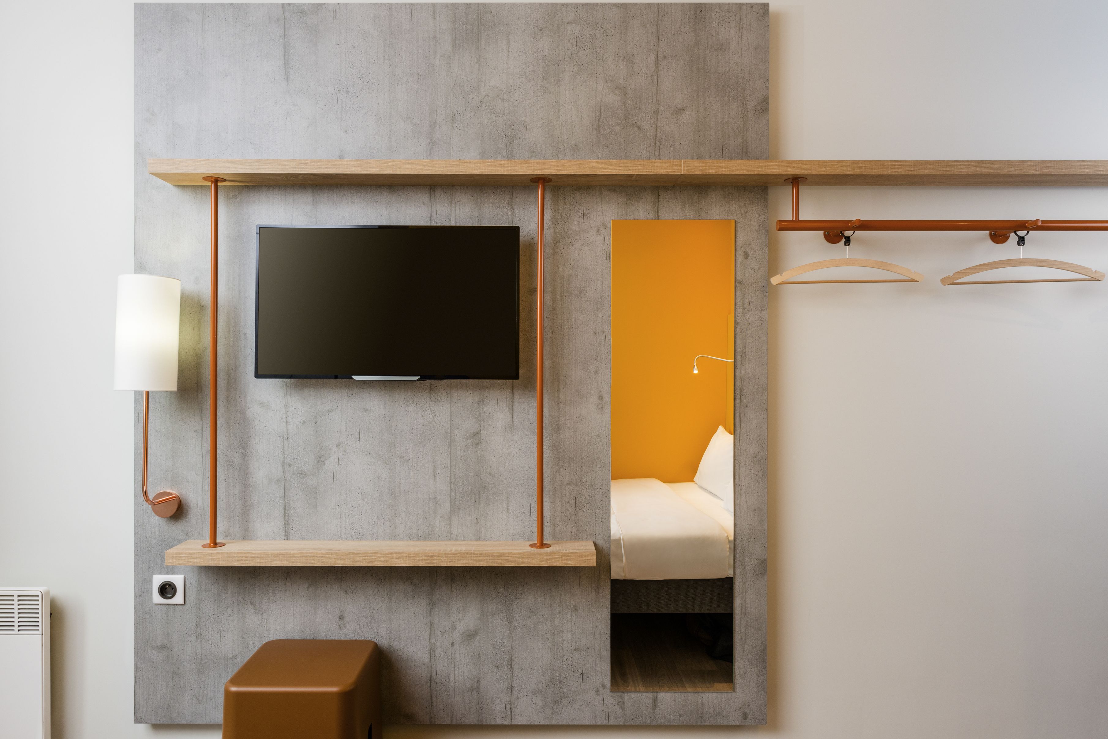 Een moderne kamer met een tv aan de muur, een spiegel, nachtkastje en hanglamp.