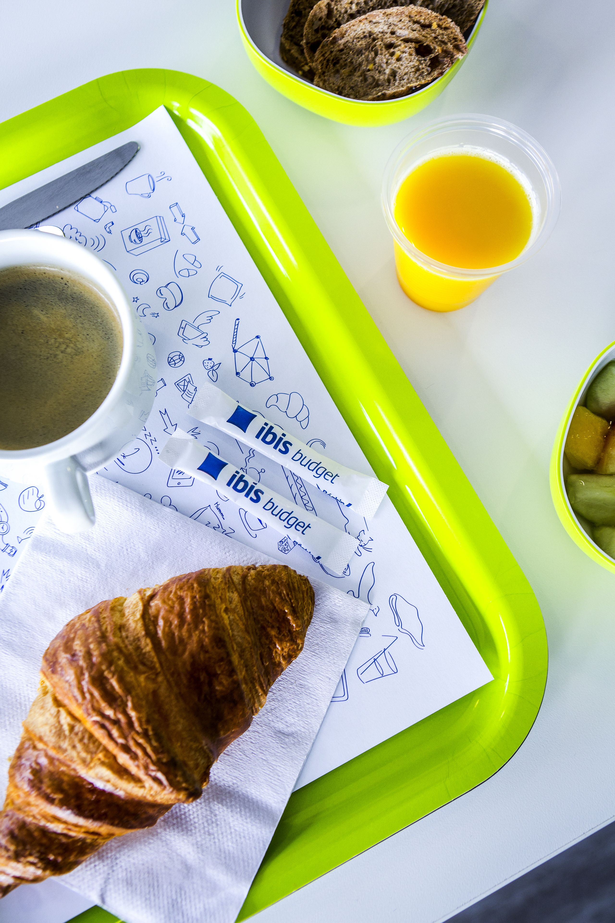 Bandeja de desayuno con un croissant, café y zumo de naranja.