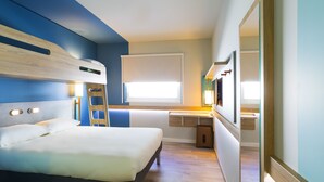 A bedroom with a bunk bed, a bedside table, a mirror, and a window with blinds. - ibis budget Marmande (Marmande)