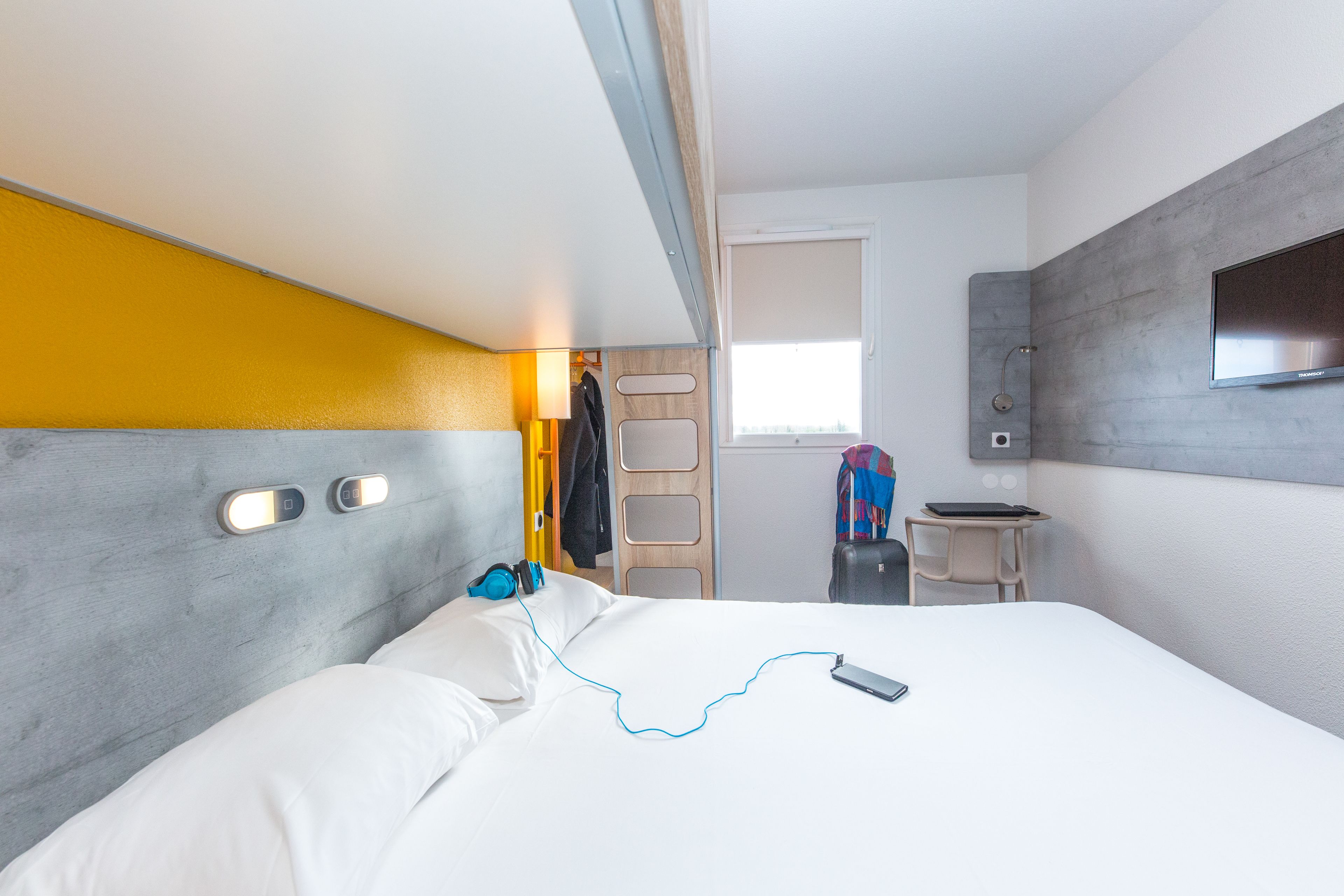 A modern hotel room with a bed, a desk, a TV, and a window.