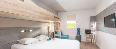 Una habitación de hotel moderna con una cama litera, un escritorio con computadora, una silla y un televisor montado en la pared.