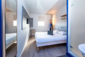 A modern hotel room with a bed, bedside table, lamp, and a TV mounted on the wall.