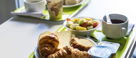 A breakfast tray with croissants, bread, fruit, yogurt, and coffee.