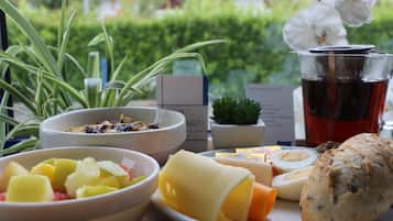Une table dressée pour le petit-déjeuner, avec des fruits, du fromage, du pain et une boisson, et une vue sur la verdure.