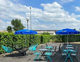 Un espacio al aire libre con sombrillas azules, sillas de metal y mesas.