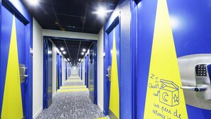 A hotel corridor with blue and yellow walls, a patterned carpet, and a door with a keypad lock. - ibis budget Marmande (Marmande)