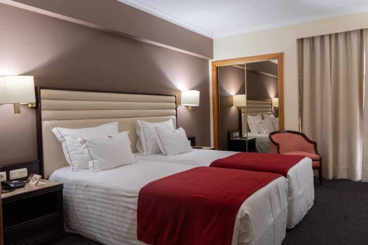 Ein Hotelzimmer mit zwei Betten, einem Nachttisch, einem Sessel und einem Spiegel.