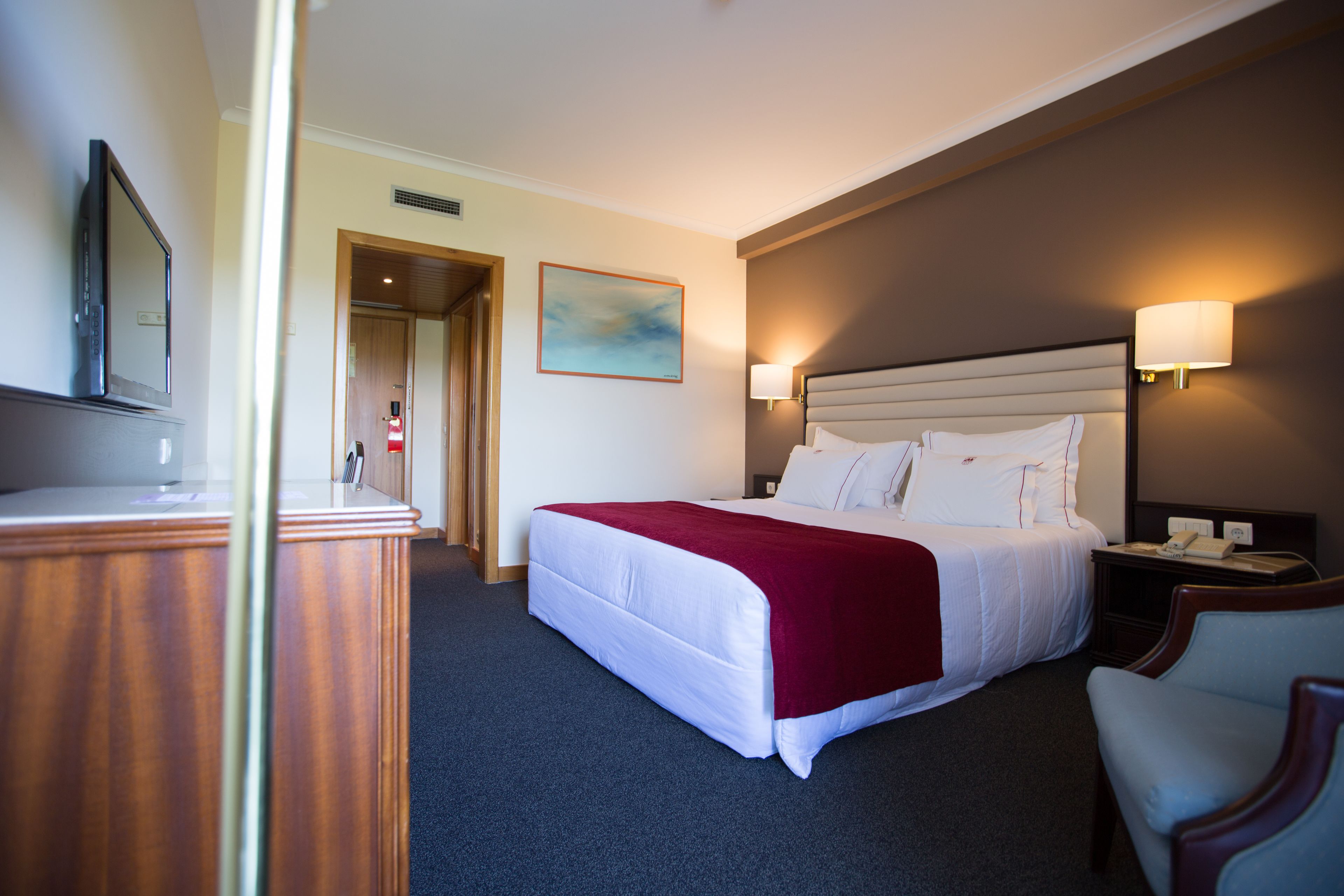 A hotel room with a bed, bedside lamps, a desk, and a television.