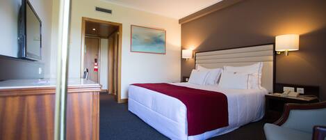 A hotel room with a bed, bedside lamps, a desk, and a television.