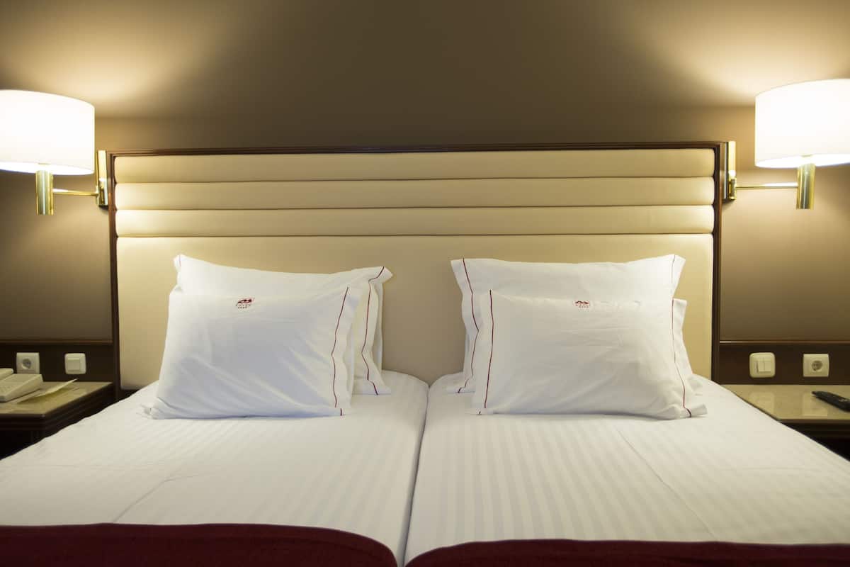 Ein Hotelzimmer mit einem großen Bett, zwei Nachttischlampen und einem Nachttisch mit Telefon und Fernbedienung.