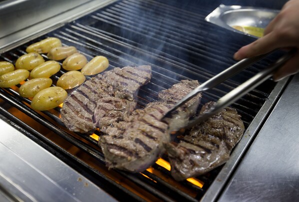 A grill with steaks and potatoes being cooked.