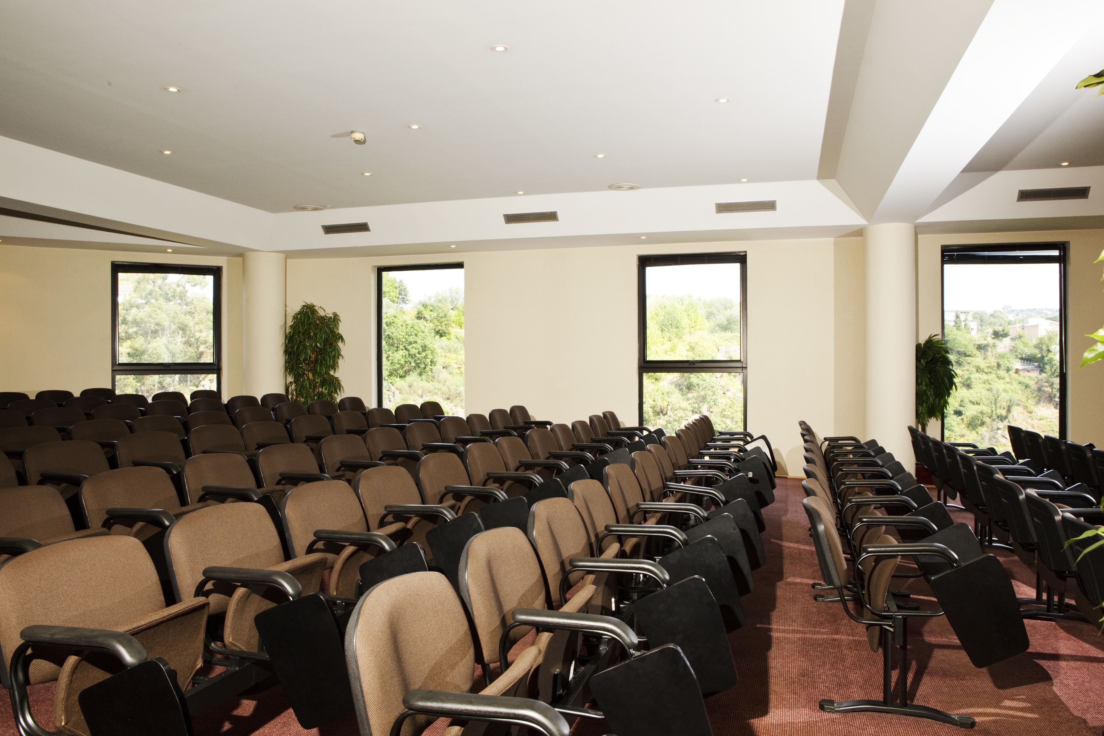 A conference room with rows of chairs, large windows, and ceiling lights.